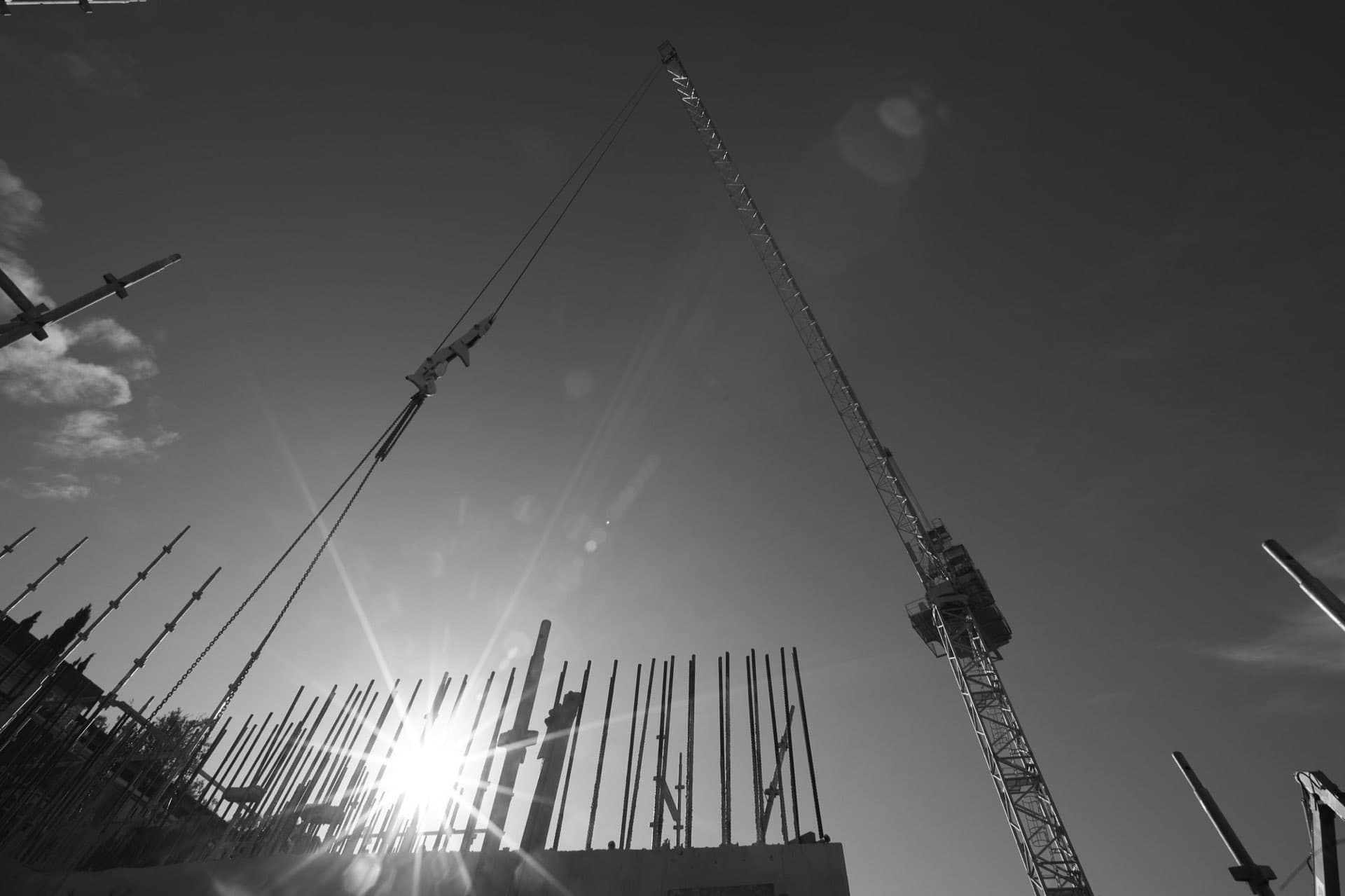 Tower crane and reinforcement steel silhouetted against the sun on a live construction site